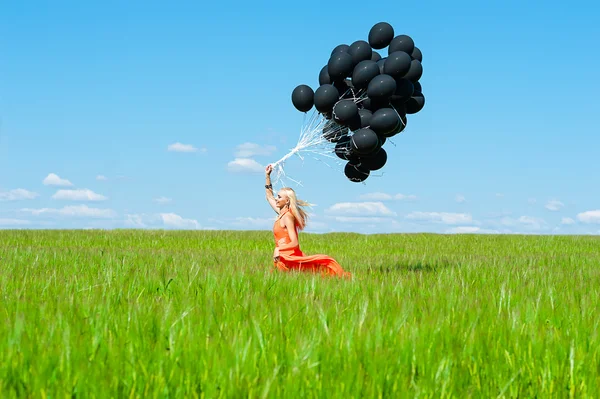 Woman with black balloons running on the green field