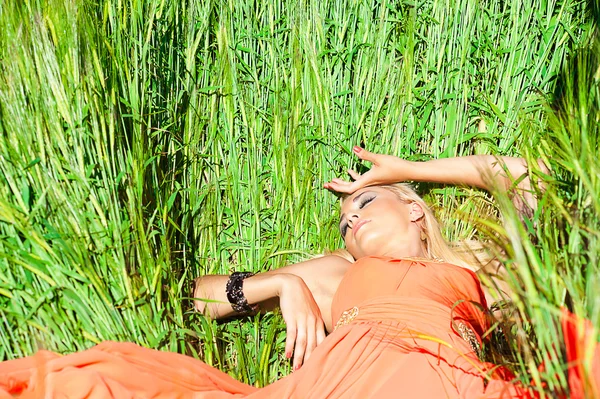 Mujer vestida de naranja acostada sobre el trigo inmaduro —  Fotos de Stock