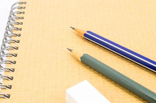 Dos lápiz de madera y goma de borrar en el cuaderno de reciclaje sobre fondo blanco . — Foto de Stock