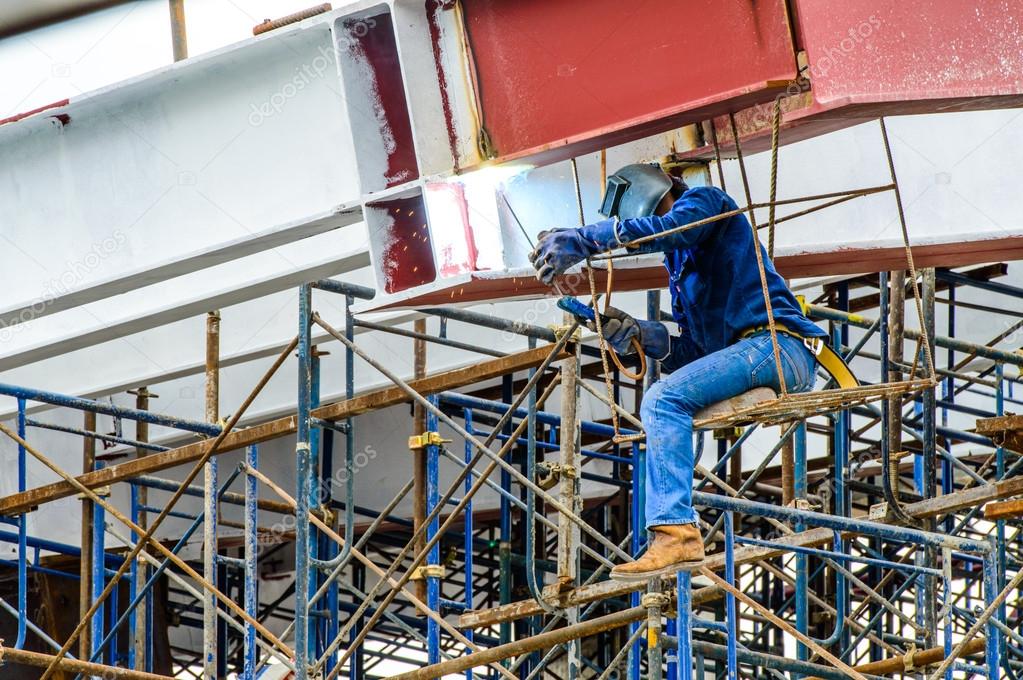 A Construction Worker welding steel bars on scaffold in construction site.