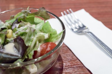 ahşap masa üzerinde bir cam kase taze salata.