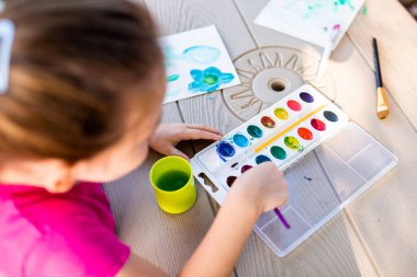 Piknik masasında kağıt üzerinde çocuk resmi. Sonbaharda dışarıda resim yapmak. Sanat projesinde çalışan kız.