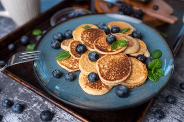 Mini pancakes on a plate with blueberries, jelly and butter. Protein pancakes for smaller bites. Diet and healthy living breakfast option. Dutch mini pancakes.