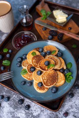 Mini pancakes on a plate with blueberries, jelly and butter. Protein pancakes for smaller bites. Diet and healthy living breakfast option. Dutch mini pancakes.