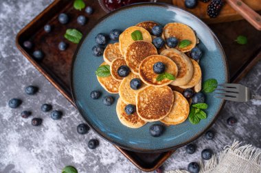 Mini pancakes on a plate with blueberries, jelly and butter. Protein pancakes for smaller bites. Diet and healthy living breakfast option. Dutch mini pancakes.