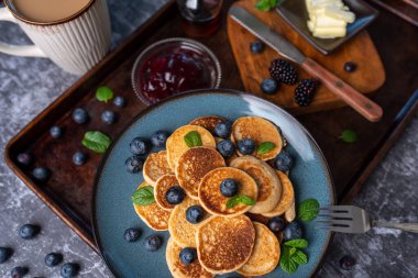 Mini pancakes on a plate with blueberries, jelly and butter. Protein pancakes for smaller bites. Diet and healthy living breakfast option. Dutch mini pancakes.