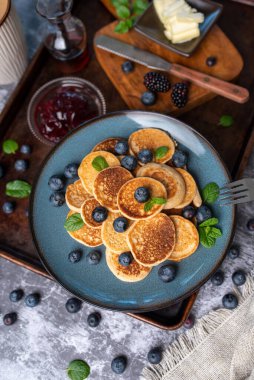 Mini pancakes on a plate with blueberries, jelly and butter. Protein pancakes for smaller bites. Diet and healthy living breakfast option. Dutch mini pancakes.