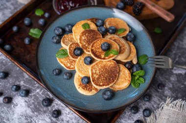 Mini pancakes on a plate with blueberries, jelly and butter. Protein pancakes for smaller bites. Diet and healthy living breakfast option. Dutch mini pancakes.