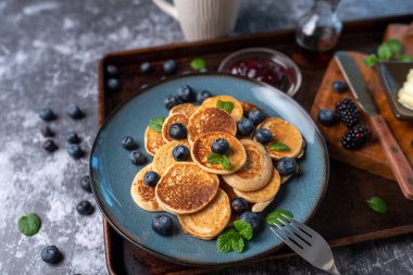 Mini pancakes on a plate with blueberries, jelly and butter. Protein pancakes for smaller bites. Diet and healthy living breakfast option. Dutch mini pancakes.