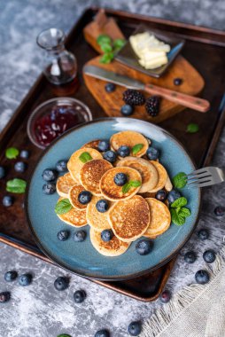 Mini pancakes on a plate with blueberries, jelly and butter. Protein pancakes for smaller bites. Diet and healthy living breakfast option. Dutch mini pancakes.
