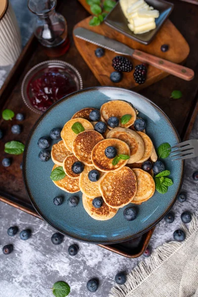 Mini pancakes on a plate with blueberries, jelly and butter. Protein pancakes for smaller bites. Diet and healthy living breakfast option. Dutch mini pancakes.