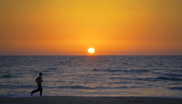 Homem correndo pelo mar ao pôr-do-sol — Fotografia de Stock