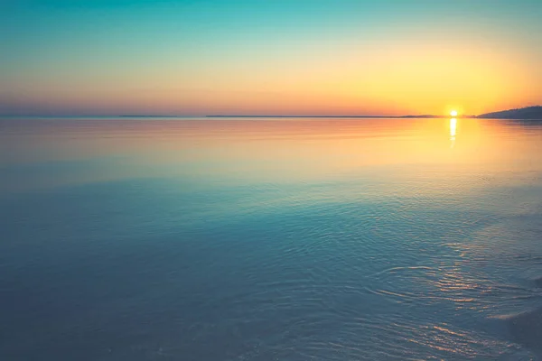 Sunset over water and coastline in the distance — Stock Photo, Image