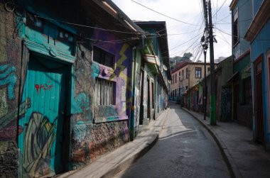 Valparaiso, Şili - Şubat 2020: Valparaiso 'da duvar yazısıyla boyanmış dar bir sokak. Valparaiso 'da sokak sanatı. Küçük caddede elektrik kabloları olan bir direk.