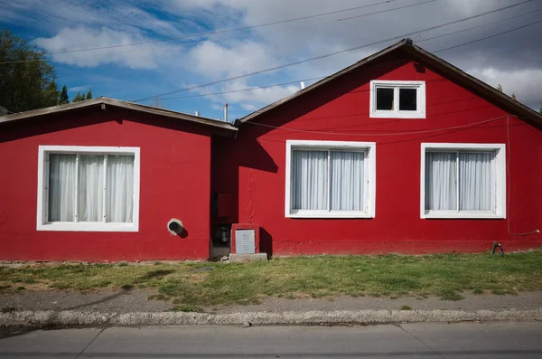 Kırmızı yüzlü, beyaz pencereli ve cadde boyunca beyaz perdeli tek katlı bir ev. El Calafate, Patagonya, Arjantin 'de küçük özel bir ev. Patagonya 'nın Arjantin bölgesinde tipik bir bina