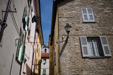 Küçük İtalyan kasabası Borgo Val di Taro 'nun ön cephesinde, pencereleri mavi panjurlu, perdeleri kapalı ve antika fenerli taş duvarlı eski bir ev. Arka planda şehir çan kulesi