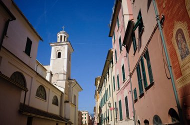 Sestri Levante kasabasındaki Nasıralı Santa Maria Bazilikası 'nın çan kulesi manzarası. Pencerelerinde ahşap panjurlar olan tipik İtalyan binaları ve cephede Bakire Meryem resmi olan dar bir sokak.