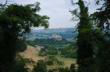 İtalya 'nın Parma eyaletindeki yemyeşil yapraklar yoluyla Castello di Torrechiara adlı kaleye ve vadiye bakın. Vadideki tepe, kale, nehir ve köylerde hasat edilen tipik İtalyan manzarası.