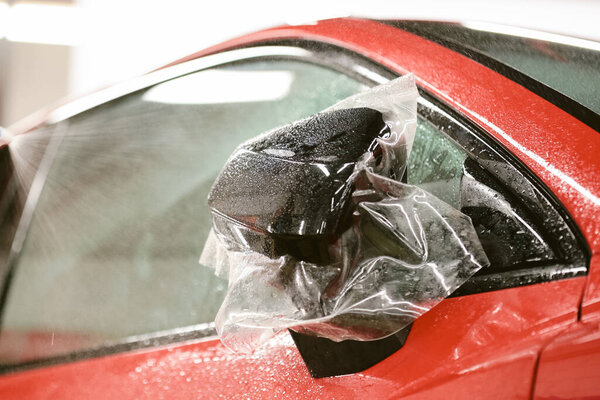 Car wrapping specialit putting vinyl foil on red car. Paint protection. Master installs film.