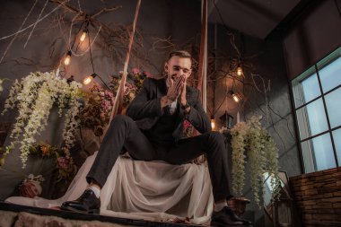 Genç yakışıklı adam salıncakta salıncakta oturuyor.