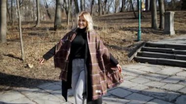 Güzel Avrupalı bir kız bahar parkı ormanında yürüyor ve daireler çiziyor, kameraya gülümsüyor, 4k yavaş çekim, güzel bebek yüzlü kadın, güneşli gün, rüzgarlı saç, mutlu gezgin, çekici güzel kadın