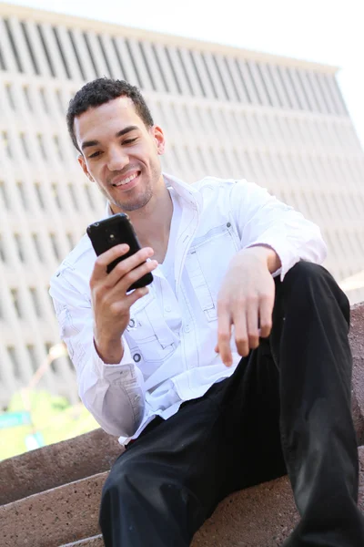 Pohledný mladý muž v bílé košili chatování na mobilním telefonu — Stock fotografie
