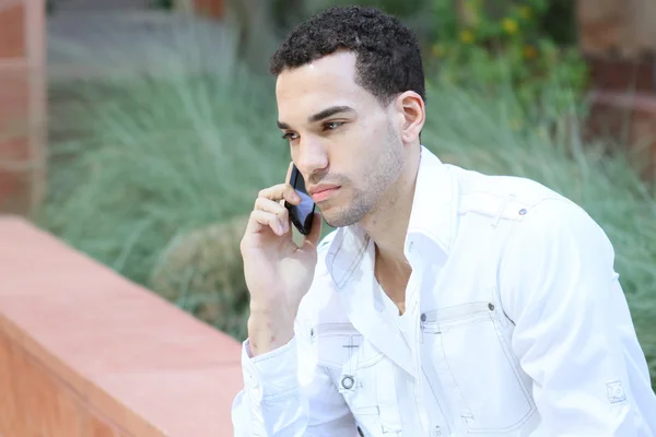 Serious young man in white shirt talking on mobile phone — Stock Photo, Image