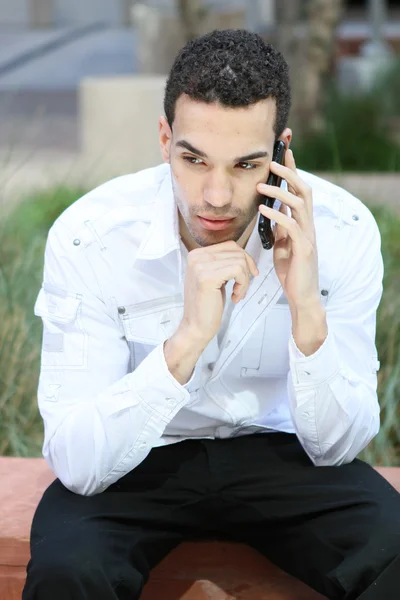 Serious young man in white shirt talking on mobile phone — Stock Photo, Image