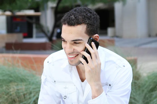 Bonito jovem sorrindo e falando no celular ao ar livre — Fotografia de Stock