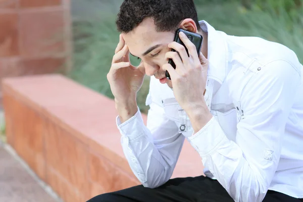 Ernstige jonge man in wit overhemd praten op mobiele telefoon Stockfoto