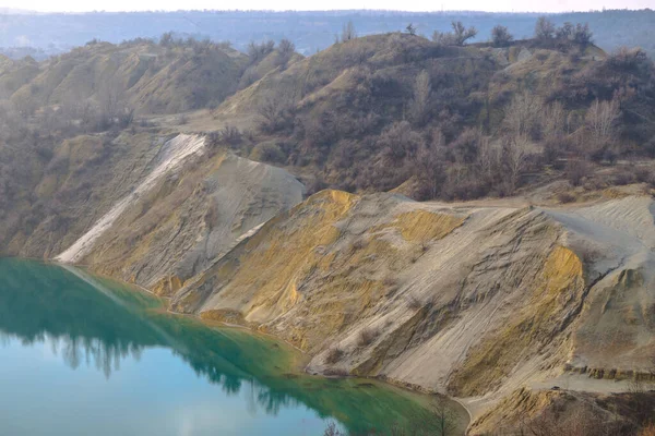 Terk edilmiş taş ocağı. Su basmış bir taş ocağı. Minerallerin çıkarılması. Kum yığınları. Çamur yamaçları. Gök mavisi