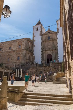 İspanya - 09: 12 2021: St. Jorge Plaza 'da manzara, San Francisco Javier Kilisesi' ni ziyaret eden turistler veya Caceres şehrinde ikonik bir miras kilisesi olan Preciosa Sangre Kilisesi