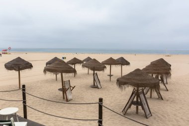 Panoramic general view of the sand of Torreira beach, empty beach, with tourist straw hats, atlantic ocean in the background, Aveiro, Portugal