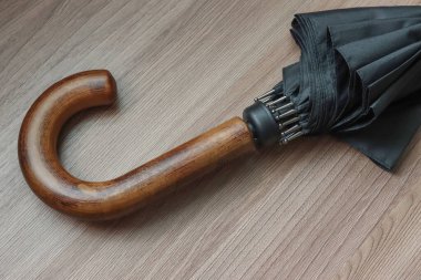 A folded black umbrella and a curved wooden handle. 