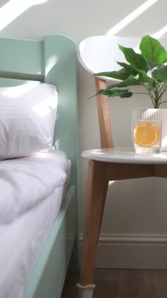 Оранжевый лимонад в стакане стоит на стуле возле кровати. Луч солнца на стене — стоковое видео