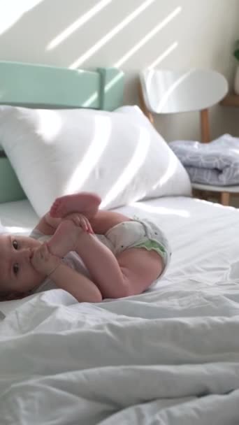 Um menino em uma fralda jaz na roupa de cama branca em uma cama grande — Vídeo de Stock