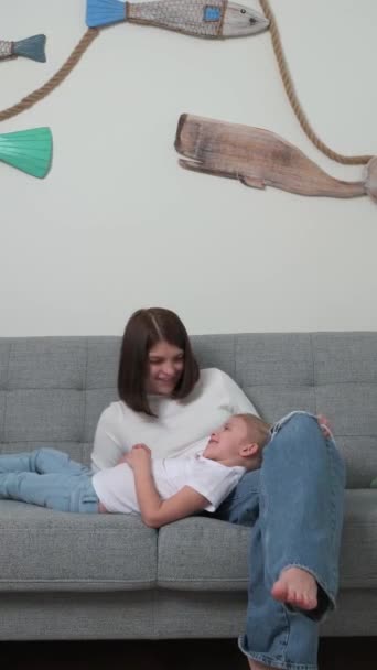 Молодая мать с маленькой блондинкой дочь сидит в комнате на диване — стоковое видео