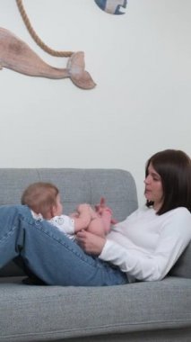 Genç, siyah saçlı bir anne ve küçük bir oğlu parlak bir odada gri bir kanepede yatıyor.