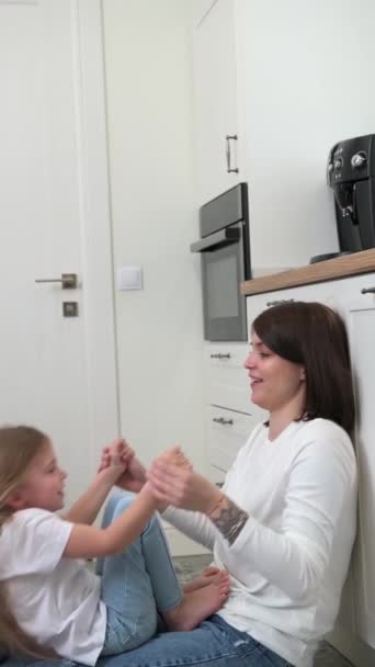 Una madre con una hija rubia se sienta y habla en el suelo de la cocina — Vídeos de Stock