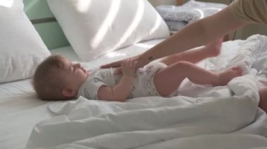 Altında bez olan küçük bir çocuk beyaz bir yatakta yatıyor, arka planda nane rengi bir yatak var..