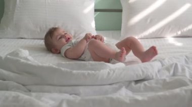 Altında bez olan küçük bir çocuk beyaz bir yatakta yatıyor, arka planda nane rengi bir yatak var..
