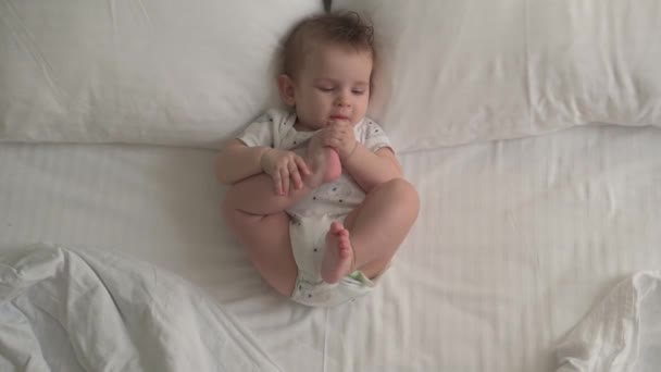 Uitzicht vanaf de bovenkant op een baby in een luier op een wit bed — Stockvideo