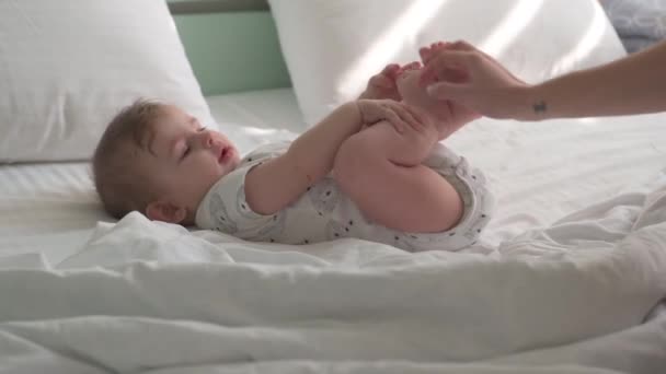Seorang anak kecil dengan popok terletak di tempat tidur putih, dengan tempat tidur berwarna mint di latar belakang. — Stok Video