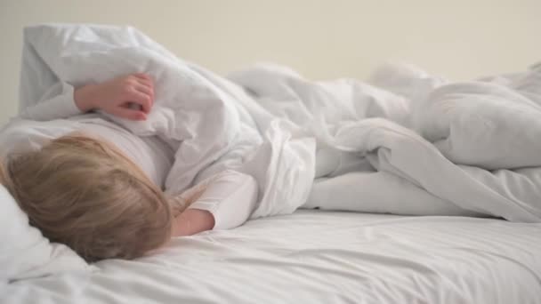 Una niña rubia de 4 años duerme en una cama blanca en los rayos del sol en la pared — Vídeo de stock