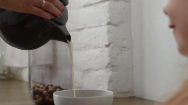 close-up of mother's hands pouring milk into a bowl of breakfast cereal for a little girl in a white kitchen. High quality FullHD footage