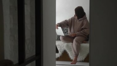 Genç bir kızın parlak bir odada oturup dizüstü bilgisayarda çalıştığı ve bilgisayarı açtığı gözetleme açısı.