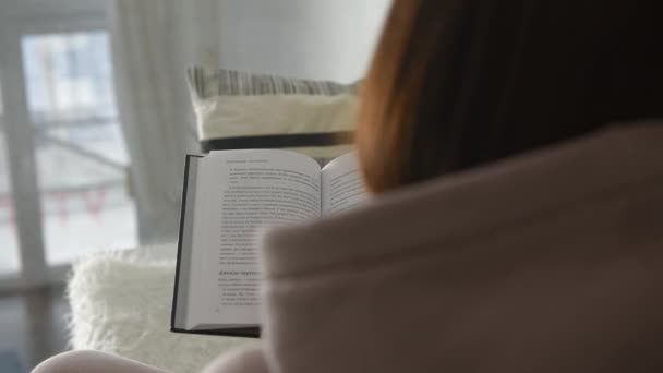 In the white interior, the girl reads a book and turns the pages of the rear view — Vídeo de Stock