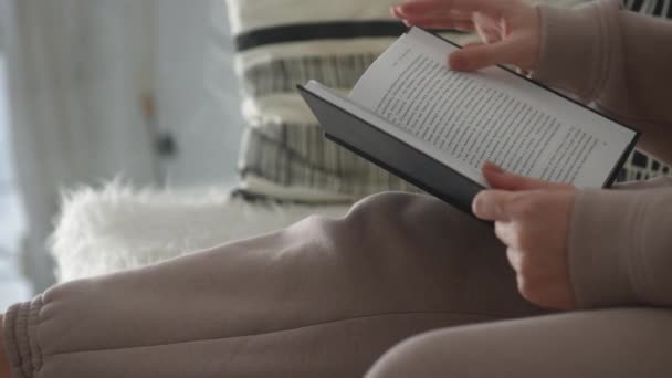 В белом интерьере девочка читает книгу и переворачивает страницы заднего вида — стоковое видео