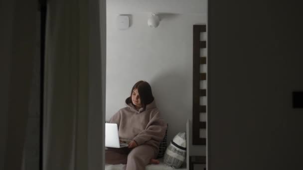 Un ángulo de visión donde una joven se sienta en una habitación luminosa y trabaja en un ordenador portátil y lo cierra — Vídeos de Stock