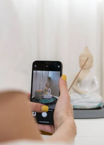 Bir kız telefonunda Buda heykelciğiyle dekor kompozisyonu fotoğrafı çekiyor.